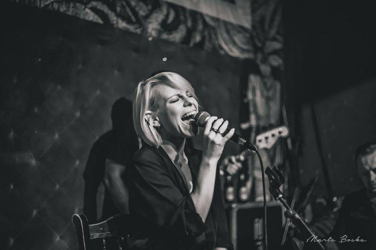Alicja Janosz śpiewa do mikrofonu na koncercie, zdjęcie czarno-białe